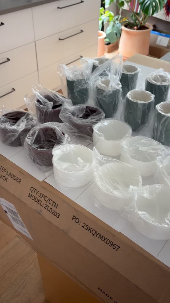 Plum, forest, and white vessels still in their sleeves on a shipping box